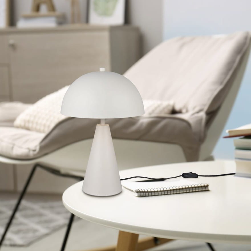 Lampa stołowa Alfie w kolorze szarym z kloszem w kształcie półkuli, umieszczona na stołowym blacie. Podstawa w formie stożka, w otoczeniu jasnego krzesła i notatnika z długopisem. Kabel z włącznikiem widoczny na stole.