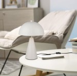 Lampa stołowa Alfie w kolorze szarym z kloszem w kształcie półkuli, umieszczona na stołowym blacie. Podstawa w formie stożka, w otoczeniu jasnego krzesła i notatnika z długopisem. Kabel z włącznikiem widoczny na stole.