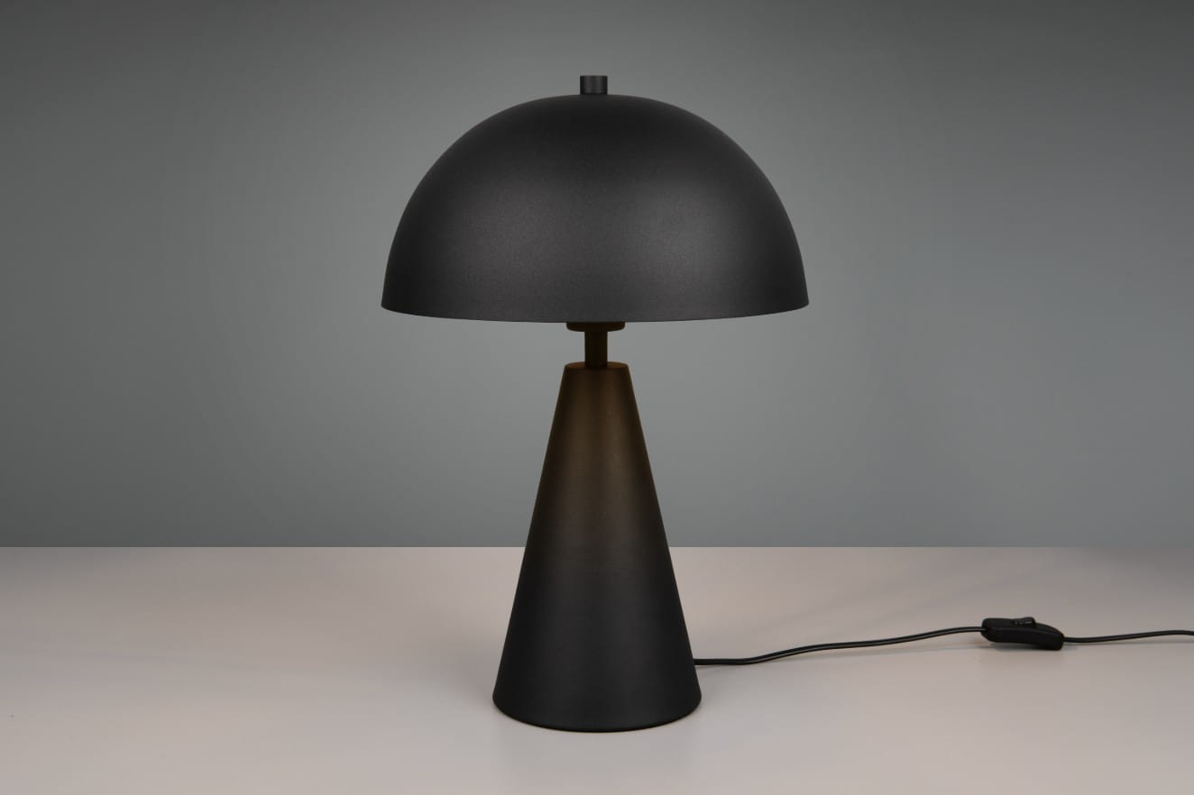 Czarna lampa stołowa Alfie z jedną oprawą E27, o cylindrycznym, stożkowatym kształcie. Górna część ma formę półkuli, a podstawa jest matowa. Produkt leży na białym stole, z widocznym kablem z włącznikiem.
