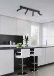 Lampa sufitowa Ambala w kolorze czarnym z czterema ruchomymi punktami LED, zamontowana na suficie. Produkt znajduje się w nowoczesnej kuchni z białymi i czarnymi szafkami oraz barowymi krzesłami. W tle widoczny stół z owocami i kwiatami.