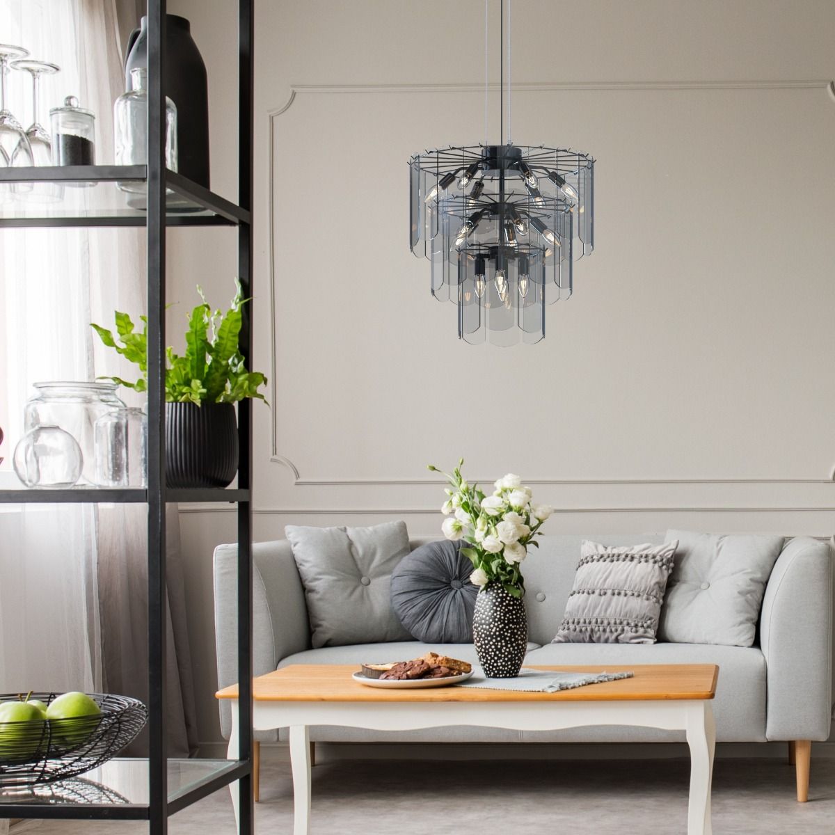 Lampa wisząca Nira w kolorze czarnym z chromowanymi detalami, z 14 miejscami na żarówki E14. Zawieszona nad jasną sofą w aranżacji salonu, z widocznymi elementami dekoracyjnymi. Szklane elementy lampy tworzą nowoczesny wygląd.