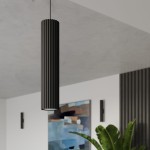 Lampa wisząca Karbon 1 w kolorze czarnym, cylindryczna z rowkowaną fakturą, z pojedynczym gniazdem GU10. Powieszona w nowoczesnym wnętrzu, w tle widoczne obrazy i rośliny. Ujęcie z dołu, ukazujące detal i stylowy design.