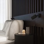 Karbon kinkiet z włącznikiem 1xGU10 w kolorze czarnym, zamontowany na ścianie za łóżkiem. Lampa o cylindrycznym kształcie z żłobieniami, skierowana w dół, obok poduszki i stolika nocnego. Tło w odcieniach ciemnego drewna, z jasnym pościelą.