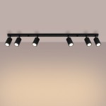 Czarna lampa sufitowa typu spot Karbon z sześcioma regulowanymi oprawami na żarówki GU10, umieszczona na prostokątnej, metalowej listwie. Kąt ujęcia frontalny, z wyraźnym układem lamp. Tło w odcieniach brązu, co podkreśla elegancki design produktu.