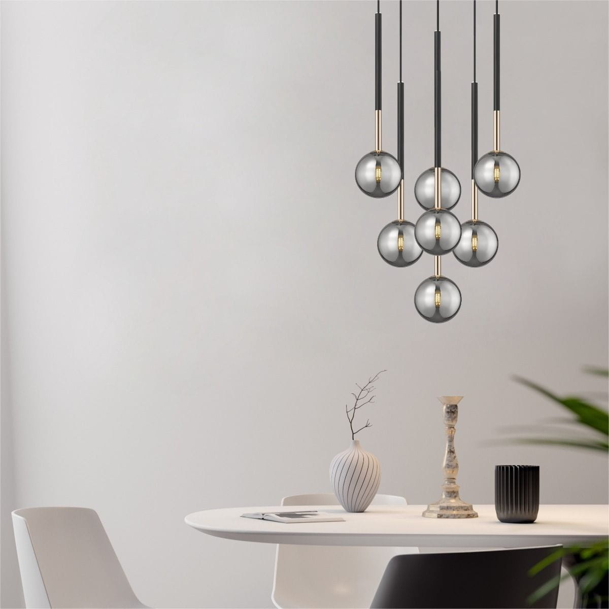 Lampa wisząca Arcturus z siedmioma kloszami G9 w kolorze czarnym i złotym. Klosze mają kulisty kształt i są zawieszone na długich, cienkich linkach. Produkt umieszczony nad okrągłym stołem w minimalistycznym wnętrzu.