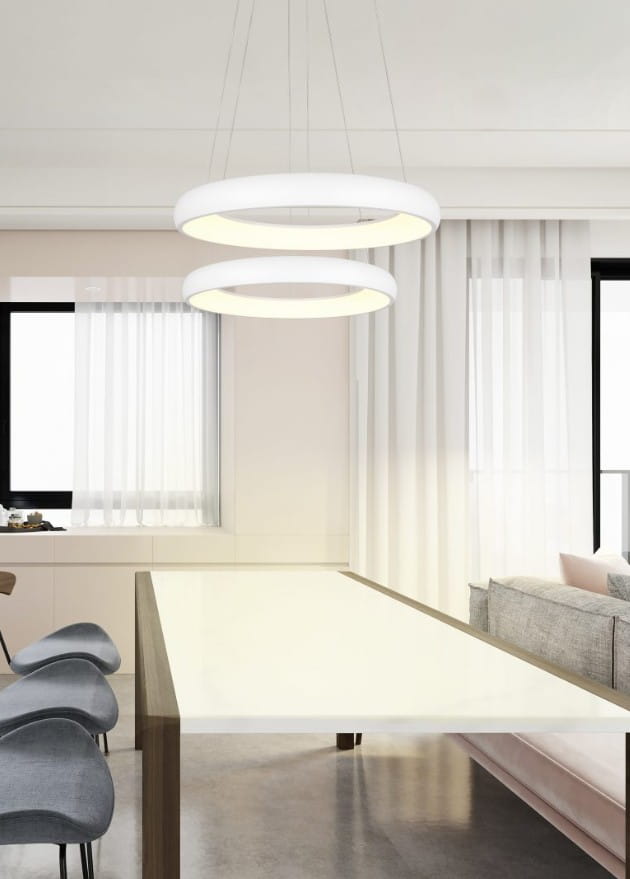 Lampa wisząca Cardona z podwójnym okrągłym kloszem w kolorze białym, zawieszona nad prostokątnym stołem. Źródło światła LED o mocy 29W, nowoczesny design. Tło z dużym oknem i zasłonami, minimalistyczne wnętrze.