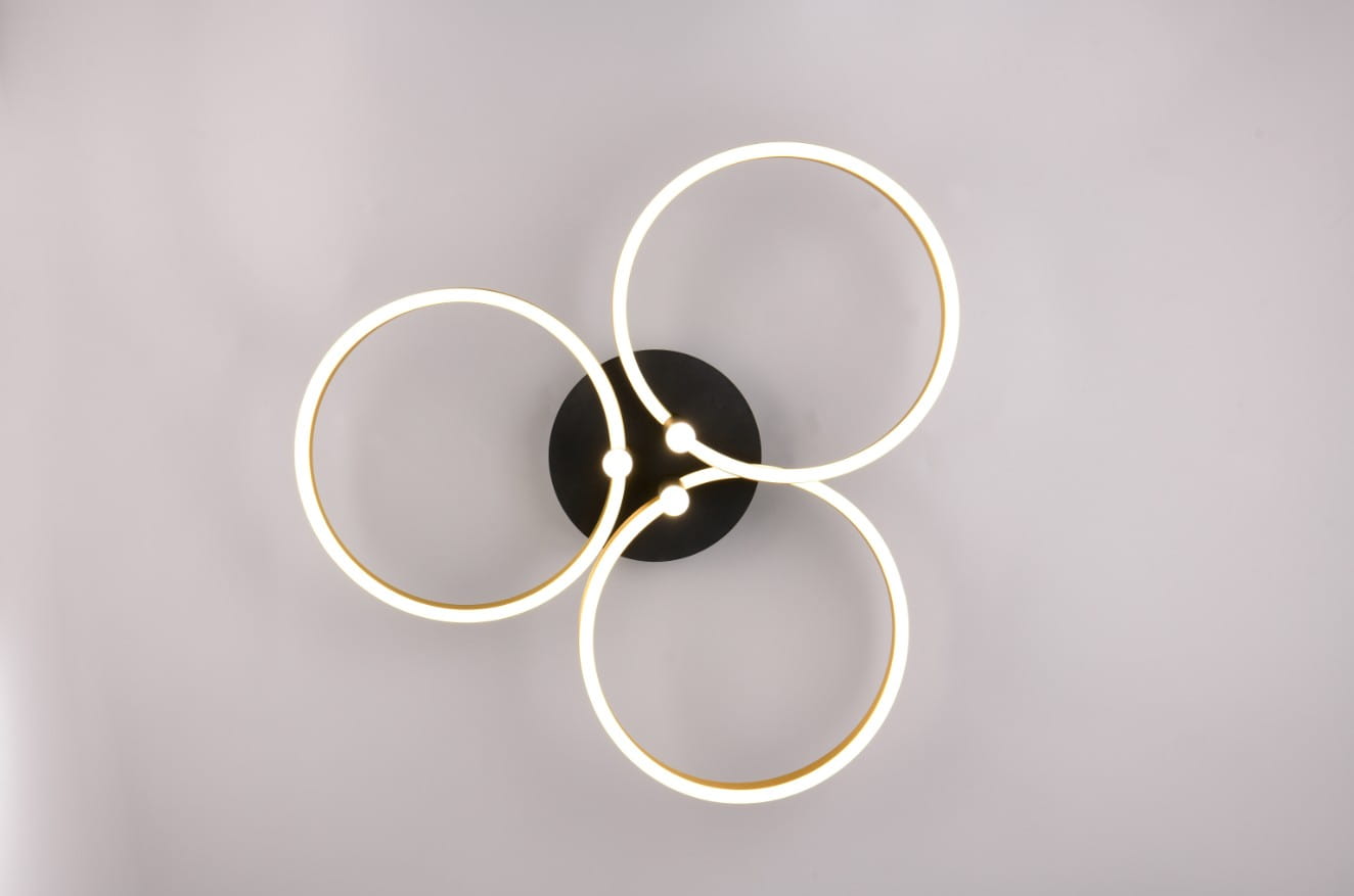 Lampa sufitowa Caruso z czarną podstawą i trzema okrągłymi pierścieniami LED w kolorze złotym. Ujęcie z góry, ukazujące symetryczny układ pierścieni, emitujących ciepłe światło. Prosta, nowoczesna forma idealna do wnętrz.