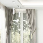 Lampa wisząca Turyn IP44 w kolorze białym, z cylindrycznym kloszem, zawieszona na cienkim przewodzie. Widoczna w aranżacji wnętrza z zasłonami w odcieniu szaro-beżowym oraz dużymi oknami, przez które wpada naturalne światło.
