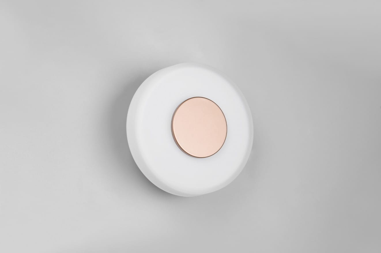 Plafon Celeste 1xLED/10W w kolorze kawowym i białym, okrągły, z białym kloszem i centralnym, metalicznym elementem w kolorze złotym. Zawieszony na gładkiej, szarej ścianie, w pozycji zamontowanej.