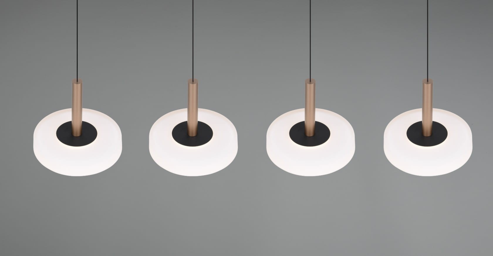 Lampa wisząca Celeste z czterema źródłami LED, o mocy 30W. Klosze w kształcie okręgów, w kolorze białym, z brązowymi metalowymi detalami i czarnym środkiem. Zawieszone na cienkich linkach, prezentują nowoczesny design. Tło jasnoszare.