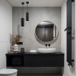 Czarna lampa wisząca Turyn IP44 z pojedynczym gniazdem GU10, zawieszona nad umywalką w nowoczesnej łazience. Lampa ma cylindryczny kształt, a jej minimalistyczny design harmonizuje z szarymi płytkami i okrągłym lustrem w drewnianej ramie.
