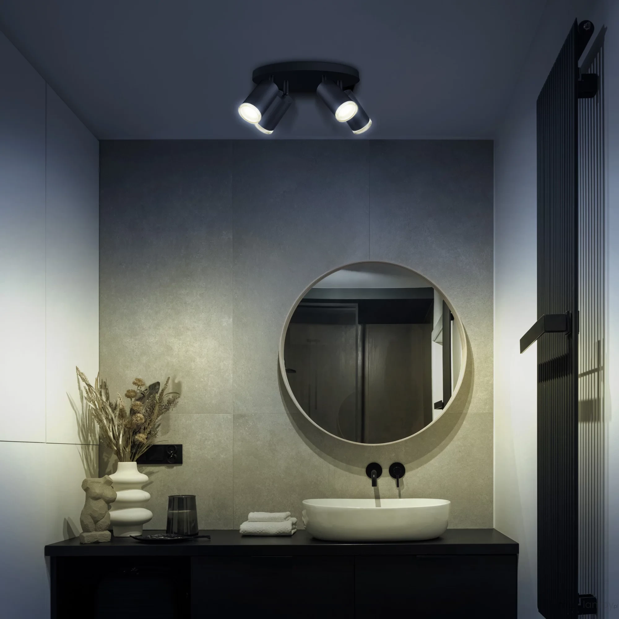 Czarna lampa sufitowa Turyn IP44 z czterema reflektorami GU10, zamontowana na suficie w nowoczesnej łazience. W tle widoczna okrągła lustro, umywalka oraz dekoracje, na przykład suszone kwiaty i figurka.