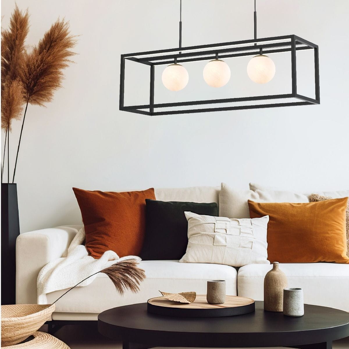 Lampa wisząca Piro w kolorze czarnym i złotym, z trzema żarówkami G9 LED, zawieszona nad stolikiem w nowoczesnym wnętrzu. W tle widoczna kanapa z poduszkami w różnych kolorach oraz dekoracje na stole.