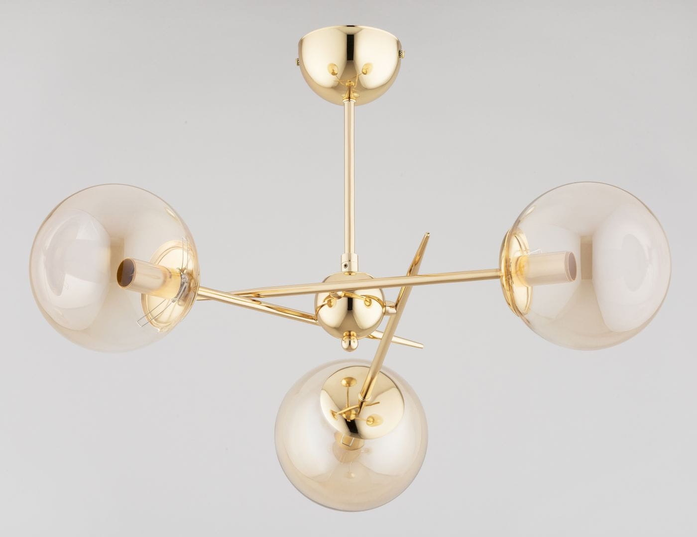Lampa wisząca Primery Gold w kolorze złotym, z trzema kloszami w kształcie kul, wykonana z przezroczystego szkła. Ułożenie na metalowej ramie z widocznymi elementami montażowymi. Produkt w pozycji wiszącej, na jednolitym tle.
