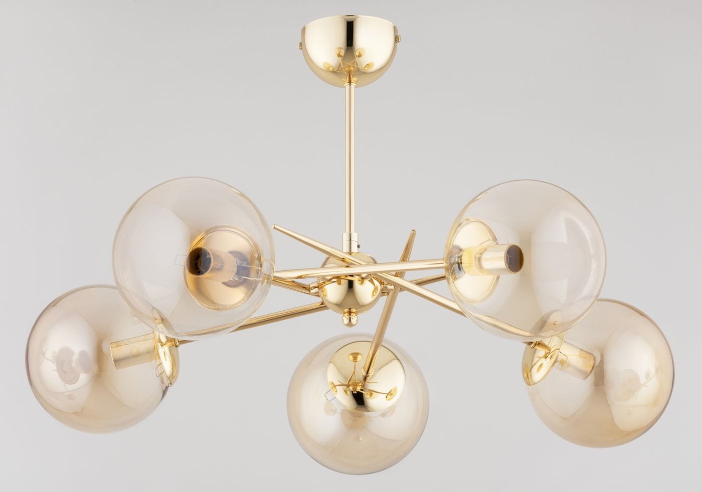 Lampa wisząca Primery Gold z pięcioma kloszami E14 w złotym wykończeniu. Klosze w kształcie kul, przezroczyste z delikatnym żółtym odcieniem, umieszczone na metalowej konstrukcji z promieniami. Montaż sufitowy, widok z dołu.