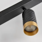 Lampa sufitowa Arras z trzema reflektorami GU10, w kolorze czarnym z ozdobnymi elementami złotymi. Widok w zbliżeniu na jeden reflektor z fakturą na powierzchni i przezroczystą żarówką. Montowana na prostokątnej, czarnej podstawie.