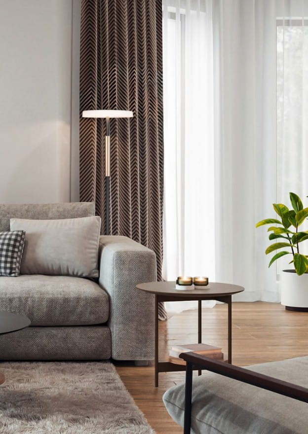 Lampa podłogowa Celeste 1xLED/15W w kolorze kawowym i białym, stojąca obok szarej sofy, z prostym, nowoczesnym designem. Widoczna w aranżacji wnętrza z zasłonami w geometryczny wzór i rośliną w doniczce.