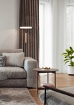Lampa podłogowa Celeste 1xLED/15W w kolorze kawowym i białym, stojąca obok szarej sofy, z prostym, nowoczesnym designem. Widoczna w aranżacji wnętrza z zasłonami w geometryczny wzór i rośliną w doniczce.