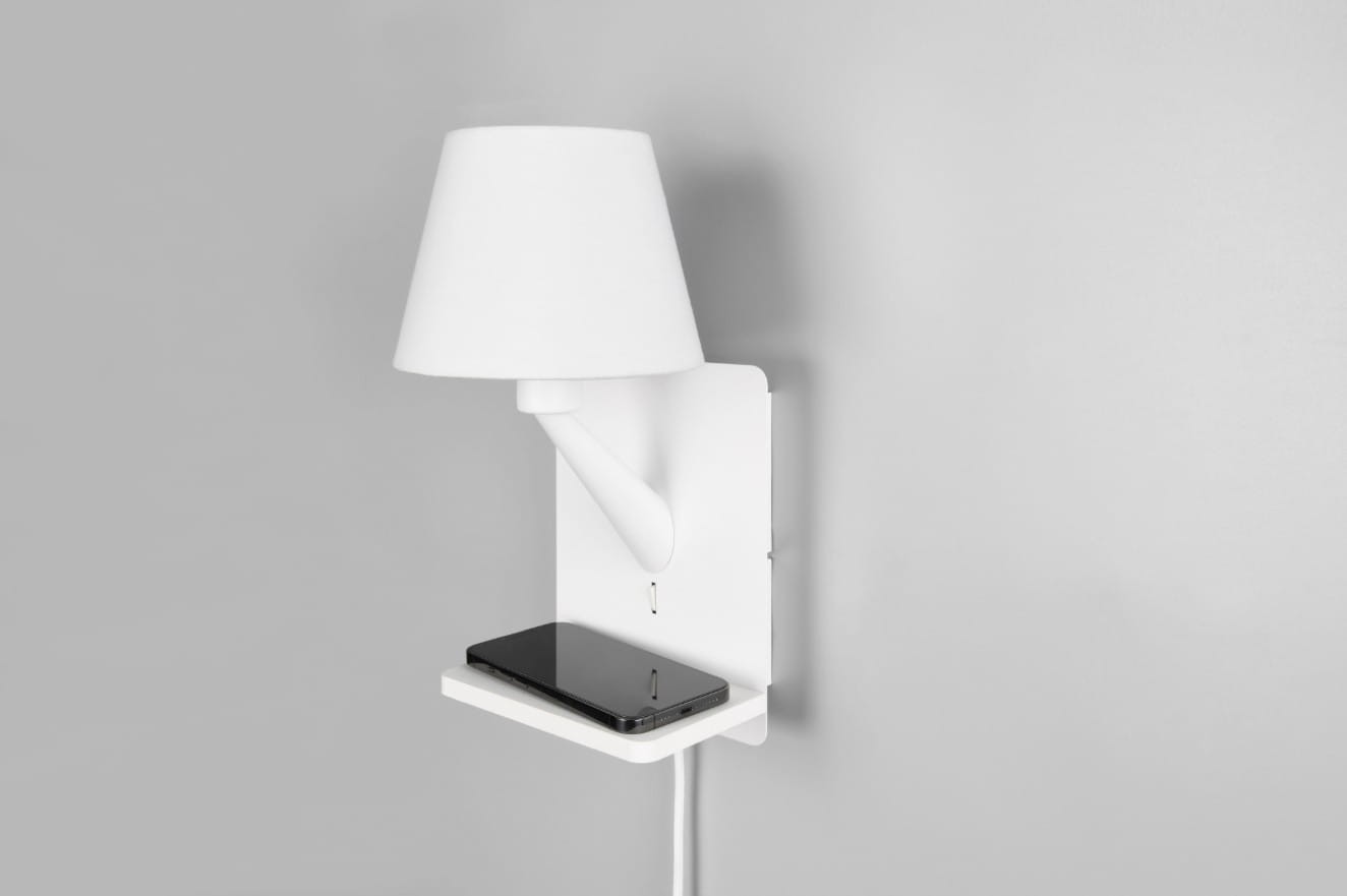 Kinkiet Comfort w kolorze białym z portem USB-C, wyposażony w abażur. Utrzymany w minimalistycznym stylu, z zamontowaną półką na telefon. Widok z boku na ścianie, z widocznym kablem zasilającym.