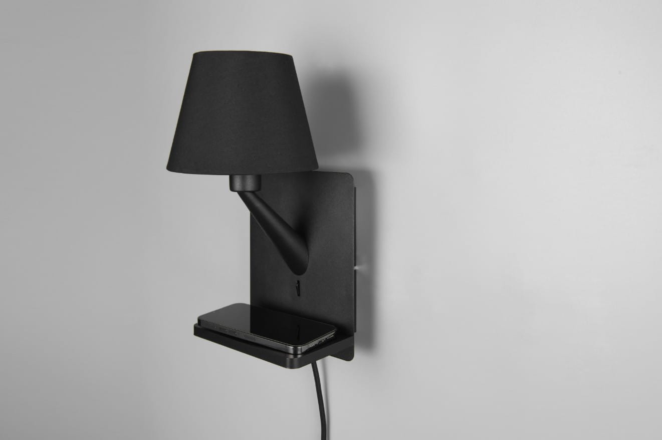 Czarny kinkiet Comfort z portem USB-C, 1xE14, zamontowany na ścianie. Ma prostą, matową podstawę i stożkowy klosz. Widoczna półka pod lampą, na której leży czarny smartfon. Kabel zasilający wychodzi z dolnej części. Tło jasnoszare.