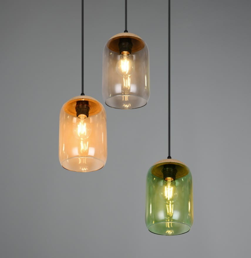 Lampa wisząca Cork z trzema kloszami w kolorach: pomarańczowym, przezroczystym i zielonym. Klasyczny design z czarnym przewodem i drewnianym wykończeniem u góry. Klosze mają zaokrąglony kształt, zawieszone w równych odstępach. Tło szare.