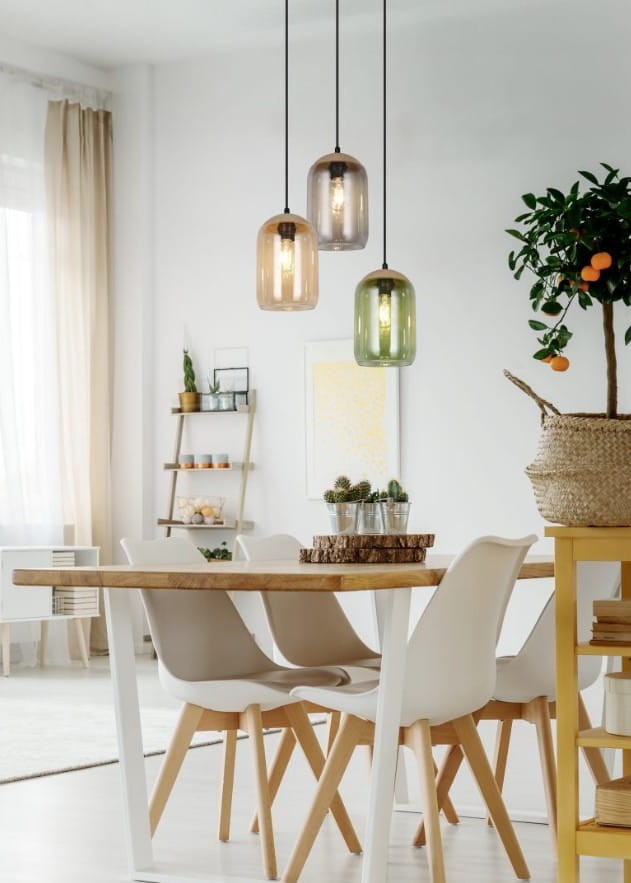 Lampa wisząca Cork z trzema kloszami w kolorach czarnym, zielonym i brązowym, zawieszona na czarnych przewodach. W tle widać drewniany stół z białymi krzesłami w nowoczesnym wnętrzu.