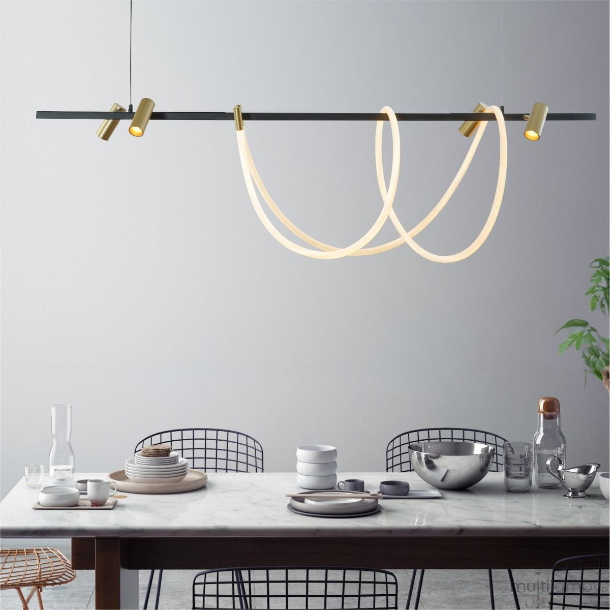 Lampa wisząca LED Balbo o mocy 45W+30W w kolorze czarnym i złotym, z elastycznymi, podświetlonymi elementami w kształcie pętli, zawieszona nad stołem w nowoczesnej aranżacji. Otoczenie z drewnianym stołem i naczyniami ceramicznymi.