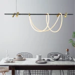 Lampa wisząca LED Balbo o mocy 45W+30W w kolorze czarnym i złotym, z elastycznymi, podświetlonymi elementami w kształcie pętli, zawieszona nad stołem w nowoczesnej aranżacji. Otoczenie z drewnianym stołem i naczyniami ceramicznymi.