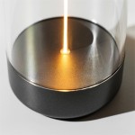 Lampa stołowa Esterno z szarym, matowym wykończeniem i przezroczystym kloszem. Widoczny zarys źródła światła LED w centralnej części podstawy. Produkt o średnicy podstawy, z efektem połysku na powierzchni.