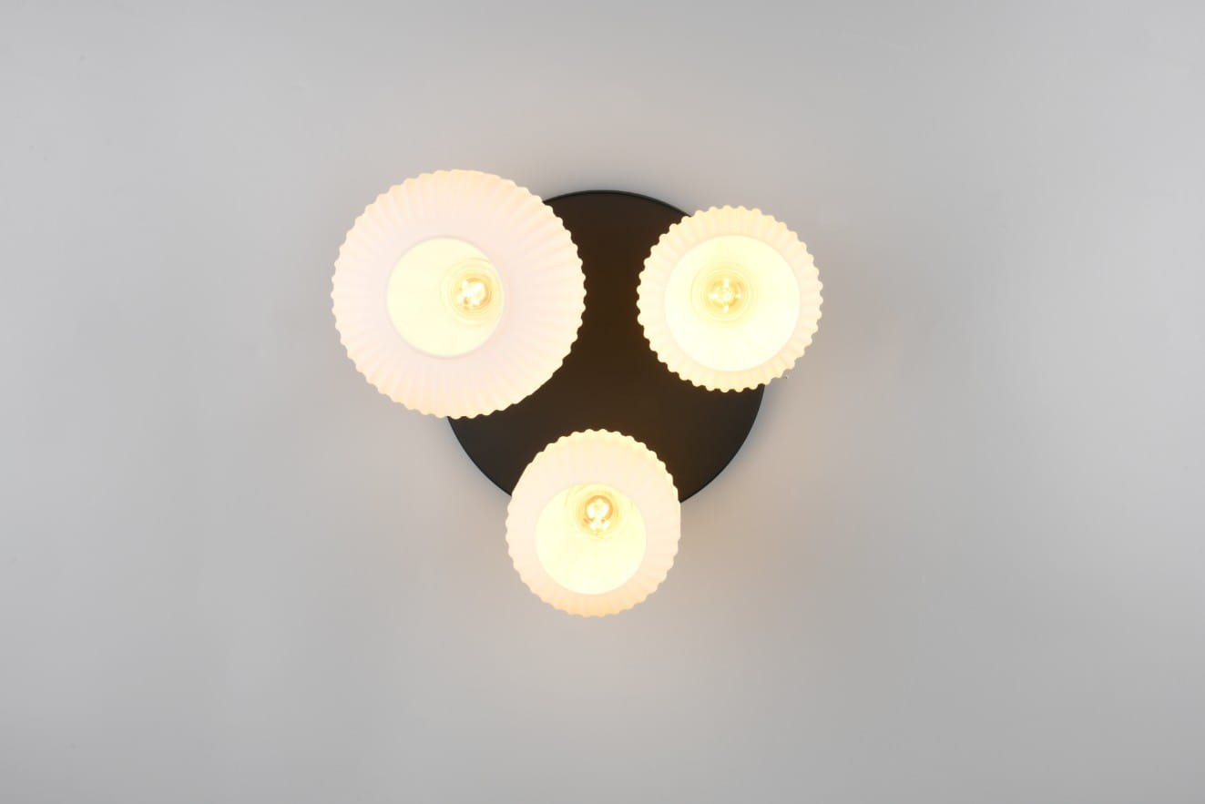 Lampa sufitowa Diva z trzema białymi kloszami o falistym kształcie na czarnej podstawie. Klosze mają miejsce na żarówki E27. Produkt zamontowany na suficie, widok z góry.
