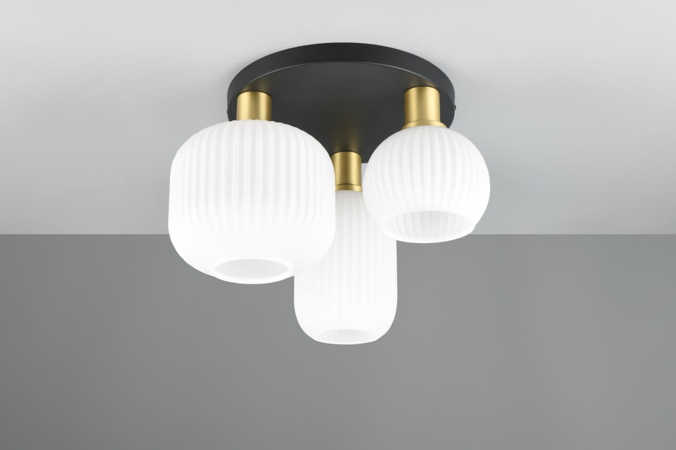 Lampa sufitowa Diva z trzema źródłami światła E27, z okrągłą czarną podstawą i białymi, teksturowanymi kloszami w kształcie cylindrów. Klosze mają złote mocowania, a całość wisi pod kątem w jasnym, minimalistycznym wnętrzu.