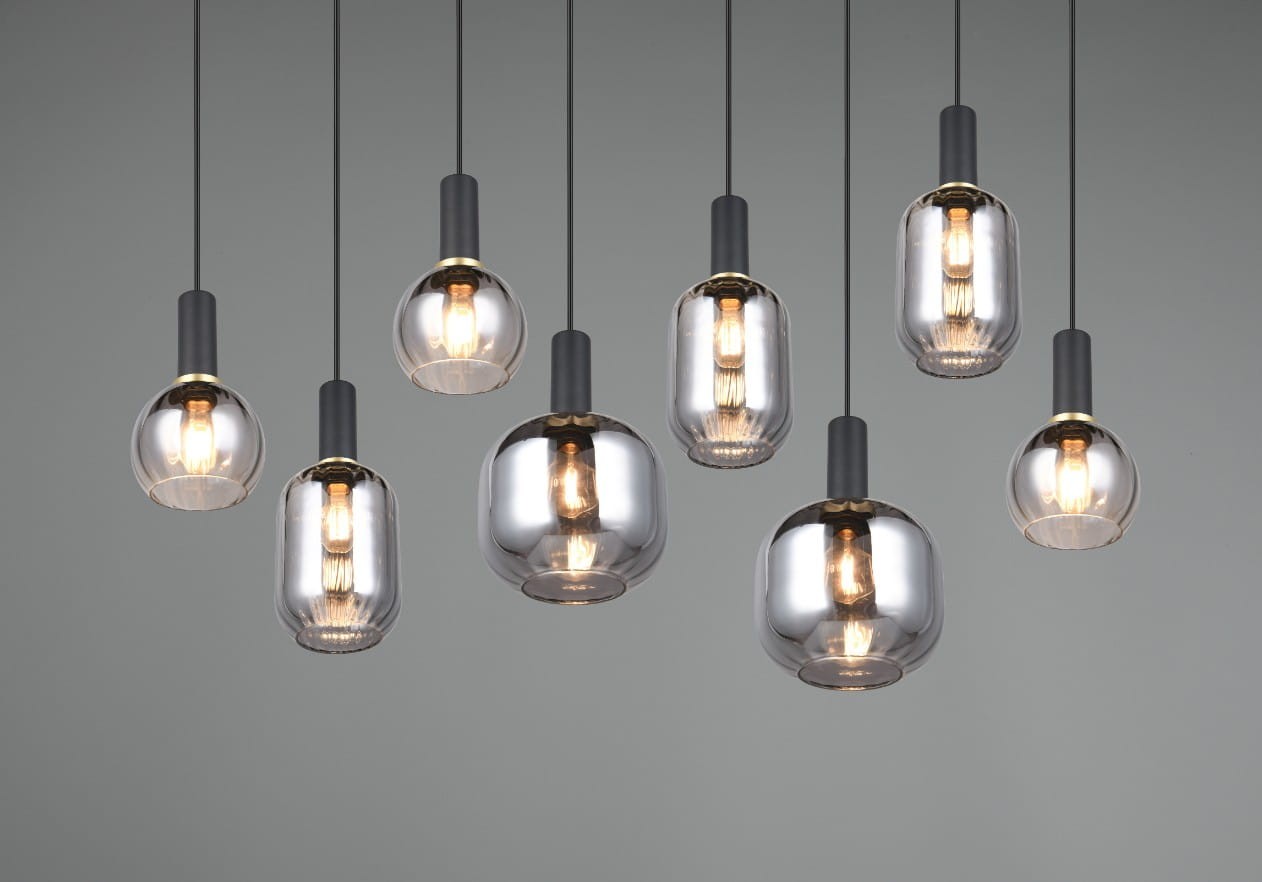 Lampa wisząca Diva z 8 oprawami E27, w kolorze czarnym i chromowanym. Wisi na cienkich kablach, z różnymi kształtami kloszy: okrągłe i cylindryczne, wykonane z przezroczystego szkła, z widocznymi żarówkami. Tło szare.