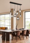 Lampa wisząca Diva w kolorze czarnym i chromowanym, z ośmioma żarówkami E27, zawieszona na prostokątnej podstawie. Wisi nad drewnianym stołem w nowoczesnym wnętrzu, z dużymi oknami w tle.
