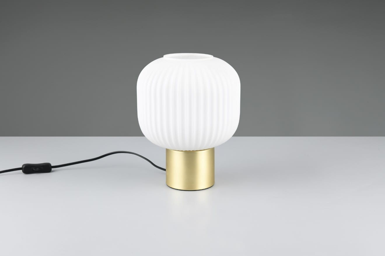 Lampa stołowa Diva 1xE27 z białym, żebrowanym kloszem z tworzywa, osadzona na mosiężnej podstawie. Widok frontalny, produkt leży na białym tle. Widoczny czarny kabel z włącznikiem.