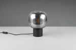 Lampa stołowa Diva z chromowaną, zaokrągloną kopułą i czarną podstawą, z widocznym gniazdem E27. Produkt leży na białym stole, z kablem z włącznikiem. Kąt ujęcia frontalny, ukazujący detale oraz fakturę lampy.