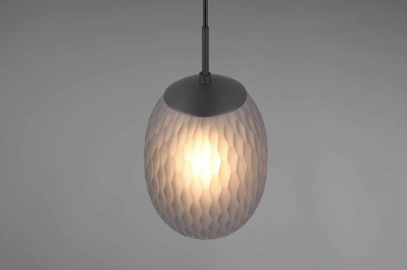 Lampa wisząca Facette z kloszem w kształcie owalu, w kolorze czarnym i przydymionym, wykonana z materiału o teksturze przypominającej plaster miodu. Zawieszona na cienkim, czarnym przewodzie, widoczna żarówka E27.