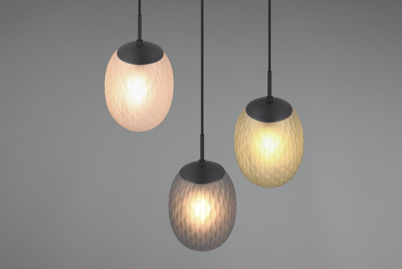 Lampa wisząca Facette z trzema kloszami w kształcie jajka, wykonana z materiału o fakturze plastra miodu. Klosze w kolorach białym, szarym i żółtym zawieszone na czarnych kablach, prezentują się na szarym tle.