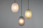Lampa wisząca Facette z trzema kloszami w kształcie owalnym, w kolorze czarnym z multikolorowymi odcieniami. Klosze mają teksturowaną powierzchnię, emitując ciepłe światło. Zawieszona na cienkich linkach, w minimalistycznym stylu.