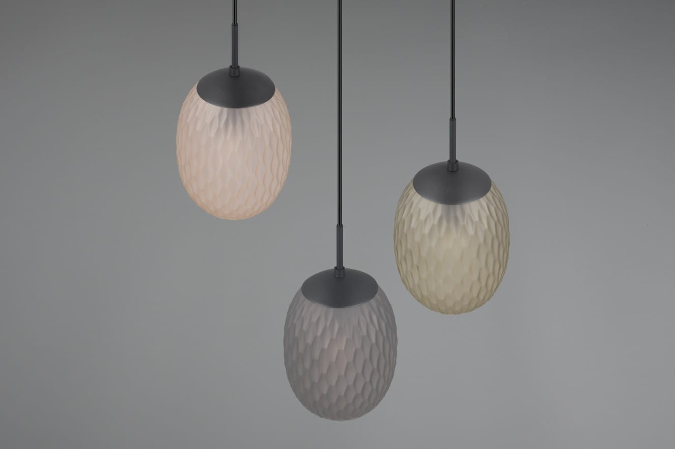 Lampa wisząca Facette z trzema kloszami w kolorze czarnym i multikolorowym, wykonana z materiału o fakturze przypominającej diament. Klosze mają owalny kształt i są zawieszone na cienkich linkach, wiszących w równych odstępach.