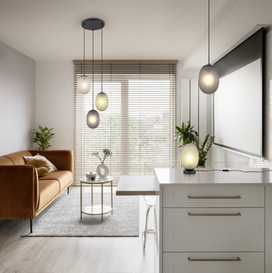Lampa wisząca Facette z trzema kloszami w kolorach czarnym i multikolorowym, zawieszona na długich kablach. Klosze mają okrągły kształt z teksturą. Lampa umieszczona w nowoczesnym wnętrzu z kanapą i stolikiem.