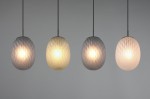 Czarna lampa wisząca Facette z czterema kloszami w multikolorze. Klosze w kształcie owalnym, wykonane z materiału o teksturowanej powierzchni, zawieszone na cienkich linkach. Oświetlenie w różnych odcieniach, tworzy efektowne źródło światła.