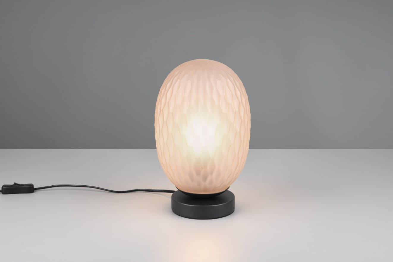 Lampa stołowa Facette z kloszem w bursztynowym kolorze, o fakturze przypominającej plastry miodu, na czarnej podstawie. Ujęcie frontalne, z widocznym kablem z włącznikiem. Idealna do nowoczesnych wnętrz. Wymaga żarówki E27.