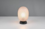 Lampa stołowa Facette w czarnej podstawie z bursztynowym, teksturowanym kloszem o kształcie owalnym. Zbliżenie na lampę włączoną, emitującą ciepłe światło, na jasnym tle. Widoczne detale tekstury klosza oraz czarna podstawa.