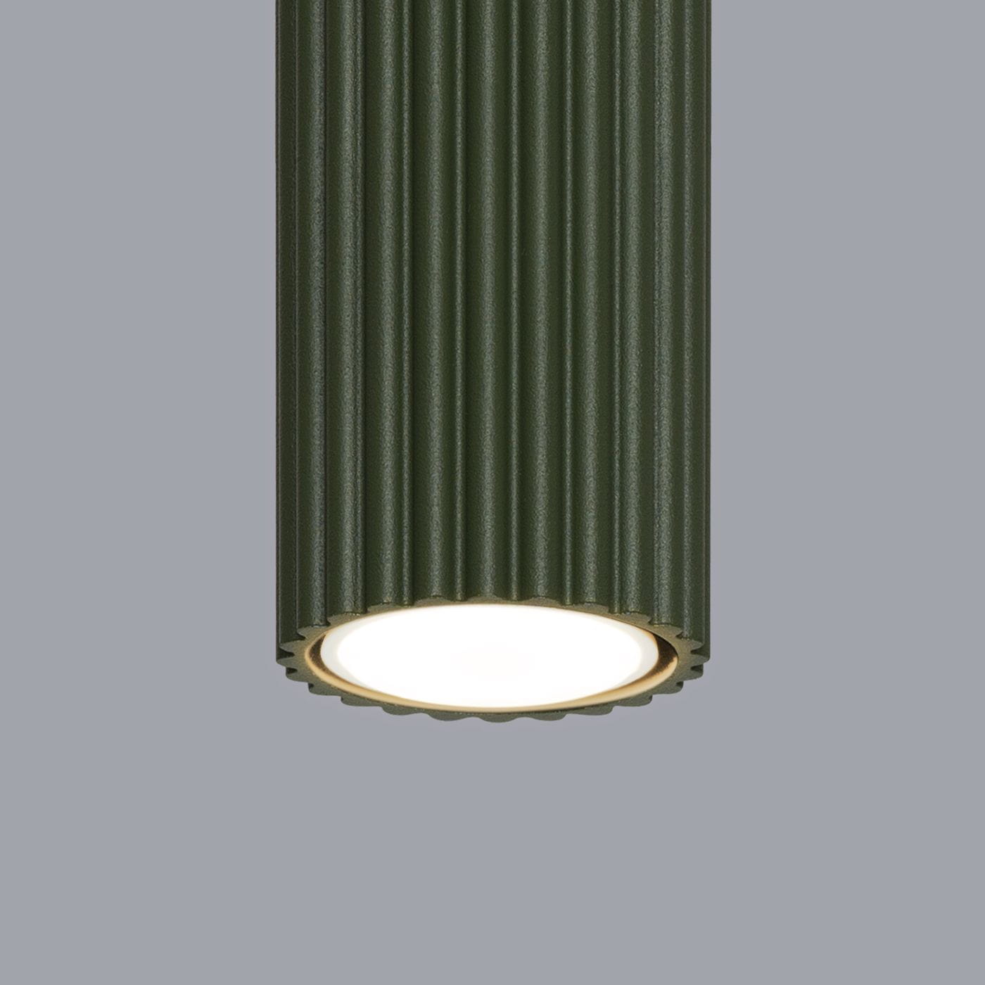 Lampa wisząca Karbon w kolorze oliwkowym z żłobioną powierzchnią. Ujęcie zbliżeniowe na oprawę z jedną żarówką GU10. Tło w odcieniu szaro-beżowym, co podkreśla elegancję lampy.