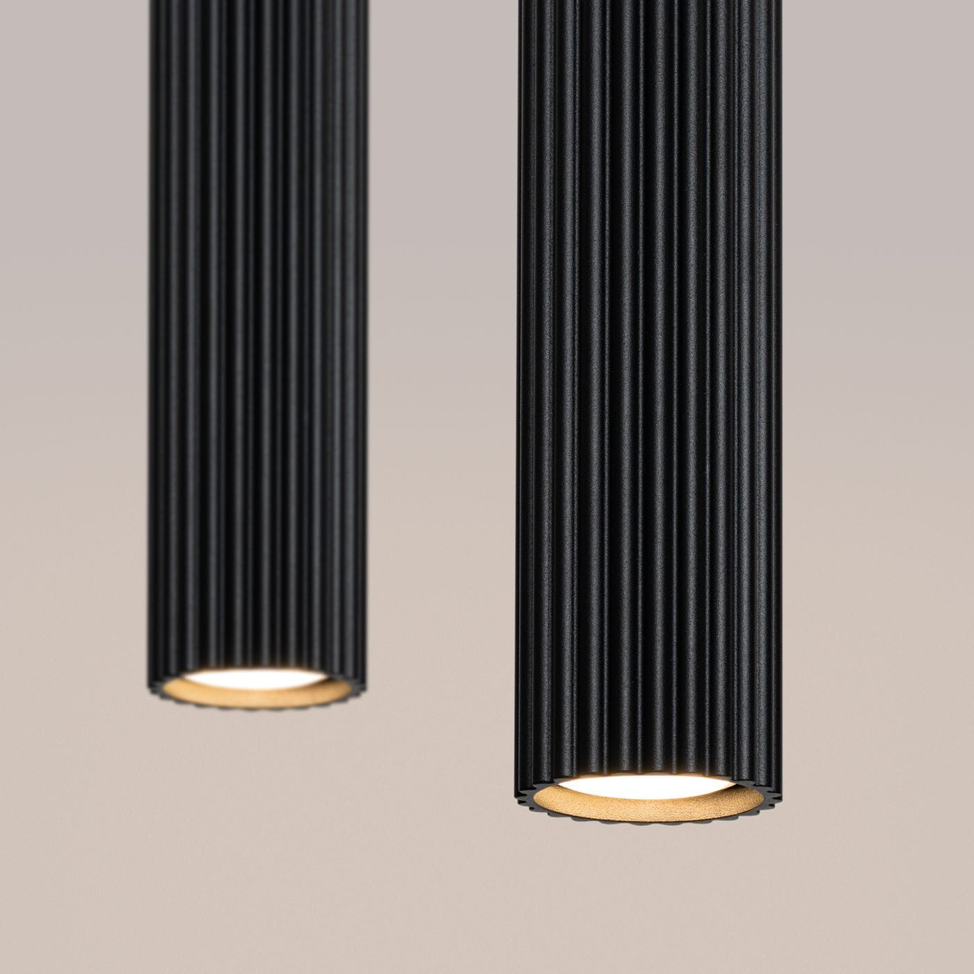 Lampa wisząca Karbon 2 z dwoma źródłami światła GU10 w kolorze czarnym. Posiada cylindryczny kształt z rowkowaną teksturą, z widocznymi kloszami u dołu, emitującymi ciepłe światło. Ujęcie z góry, na jednolitym tle.
