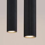 Lampa wisząca Karbon 2 z dwoma źródłami światła GU10 w kolorze czarnym. Posiada cylindryczny kształt z rowkowaną teksturą, z widocznymi kloszami u dołu, emitującymi ciepłe światło. Ujęcie z góry, na jednolitym tle.