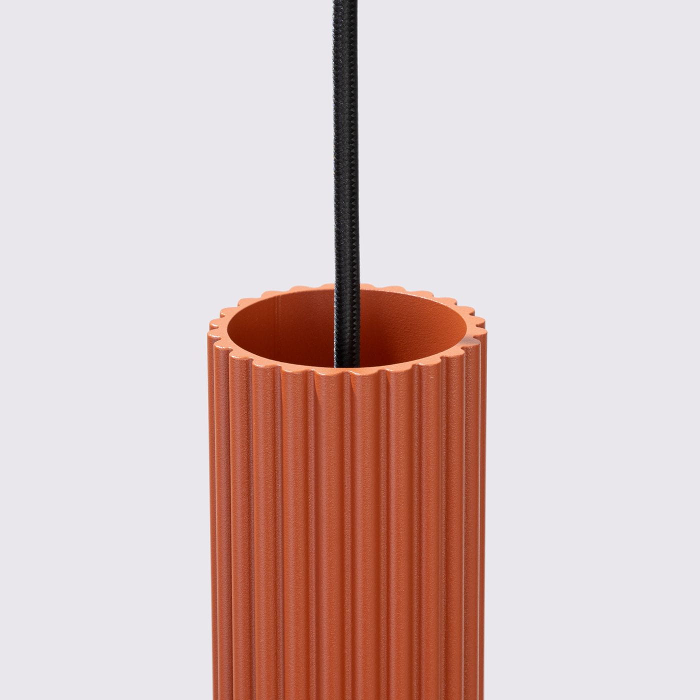 Lampa wisząca Karbon 3 w kolorze ochra czerwona, z cylindrycznym kloszem o fakturze żłobionej, z trzema gniazdami GU10. Widoczne czarne zawieszenie. Produkt zainstalowany w pozycji pionowej, na prostym tle.