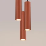 Lampa wisząca Karbon 3P w kolorze ochra czerwona z trzema cylindrycznymi kloszami o żebrowanej fakturze. Ujęcie frontalne, klosze zawieszone na czarnych przewodach, z widocznymi źródłami światła GU10. Tło w jednolitym odcieniu.