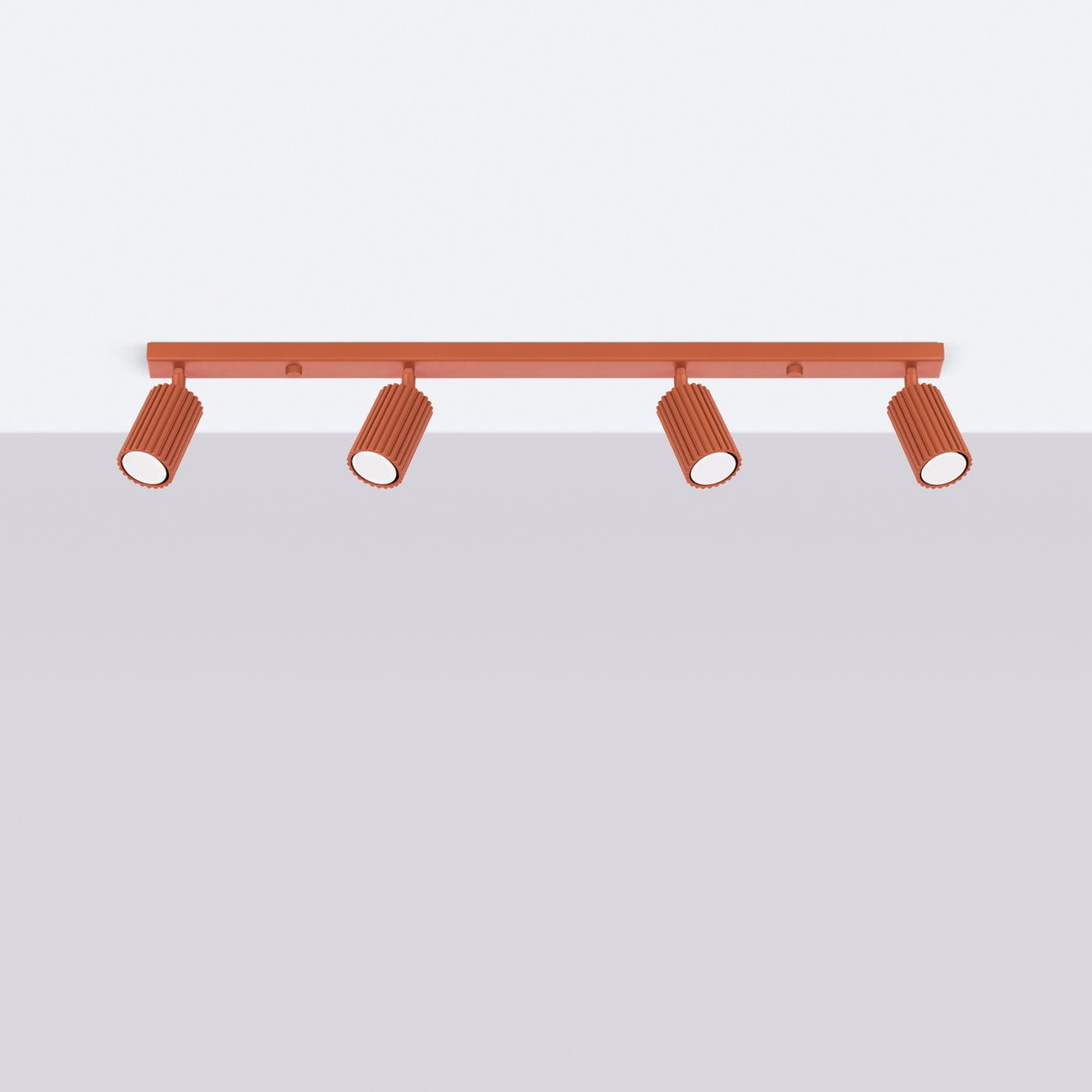 Lampa sufitowa Karbon L w kolorze ochra czerwona, z czterema reflektorami GU10. Ujęcie frontalne, lampa zamontowana na ścianie. Reflektory mają wyraźne, żłobione elementy, skierowane w dół. Proste tło, które podkreśla kolorystykę lampy.