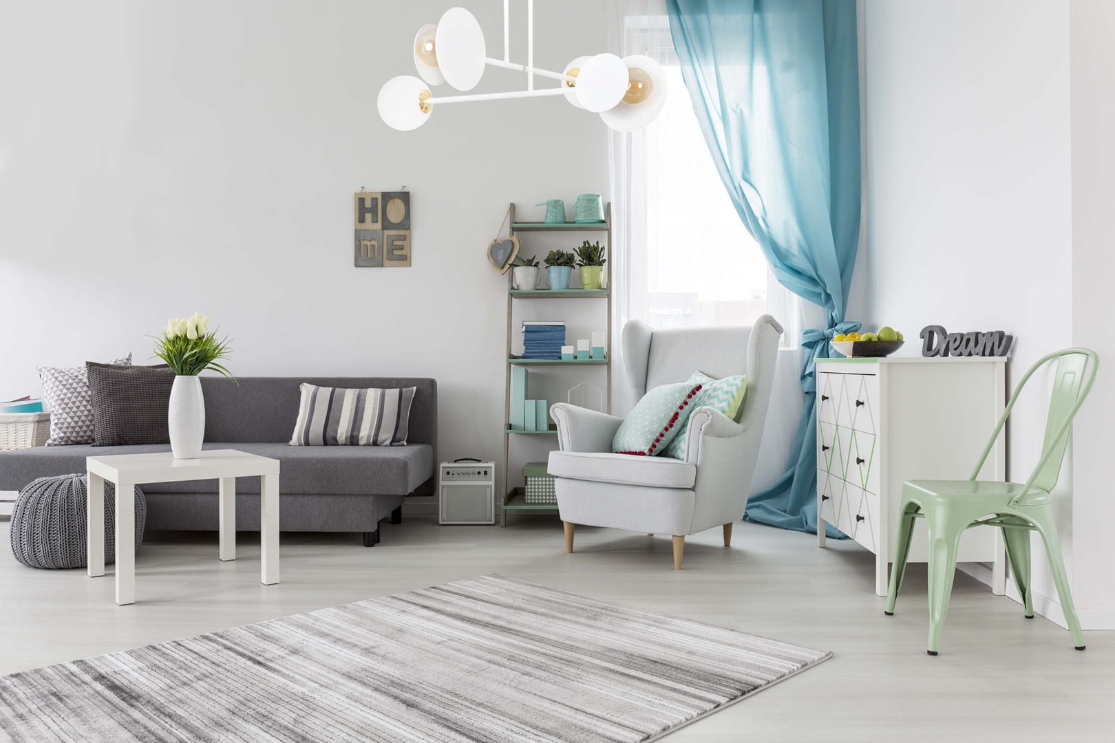 Lampa sufitowa Minerva 4-punktowa w białym kolorze, z okrągłymi kloszami, zawieszona w jasnym wnętrzu. W tle szara kanapa, stół, rośliny i dekoracje. Ujęcie frontalne pokazuje elegancki design i funkcjonalność lampy w aranżacji pomieszczenia.